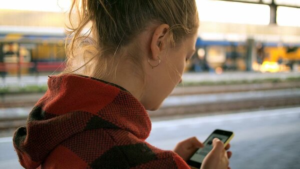 Woman in a red hoodie reading opt-in texts in a train station