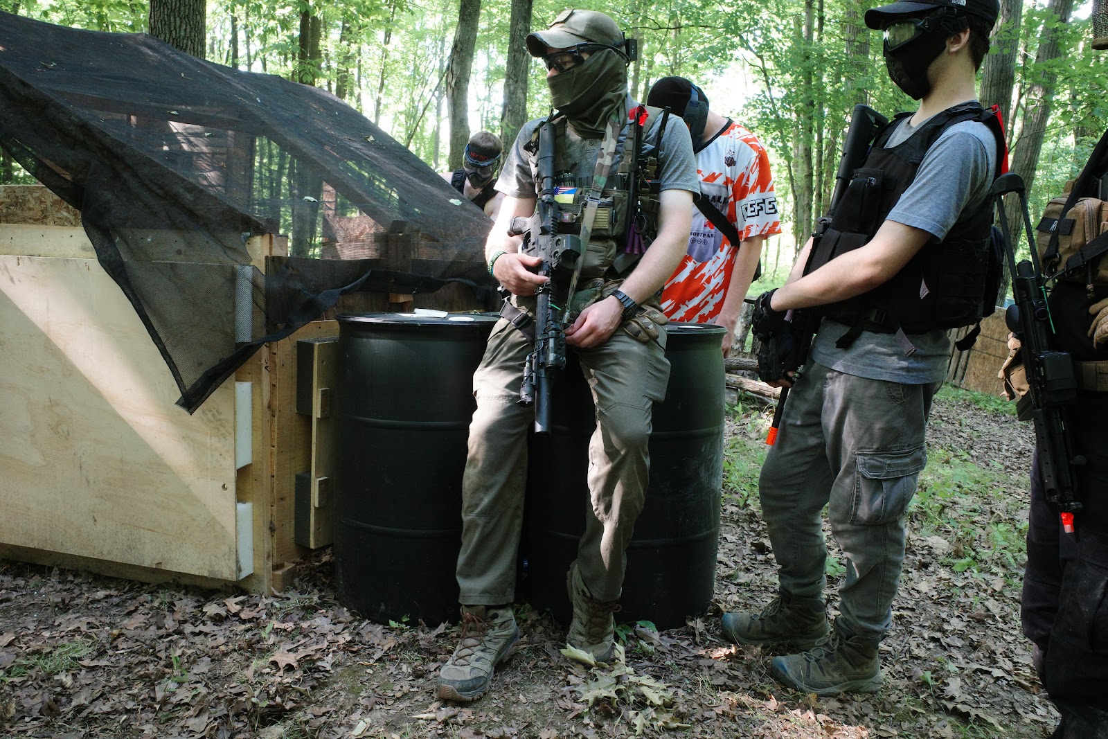 Men in full airsoft gear with airsoft rifles looking into the distance in the woods.