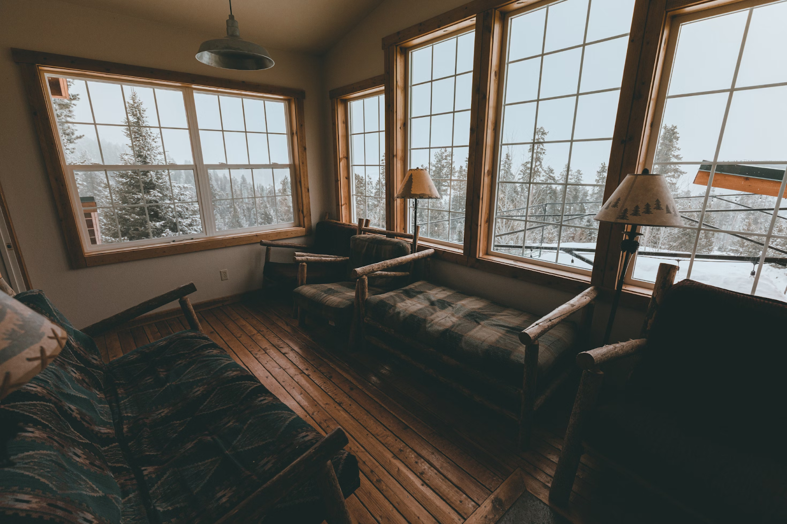 A living room has couches and chairs. Windows showcase a snowy landscape.