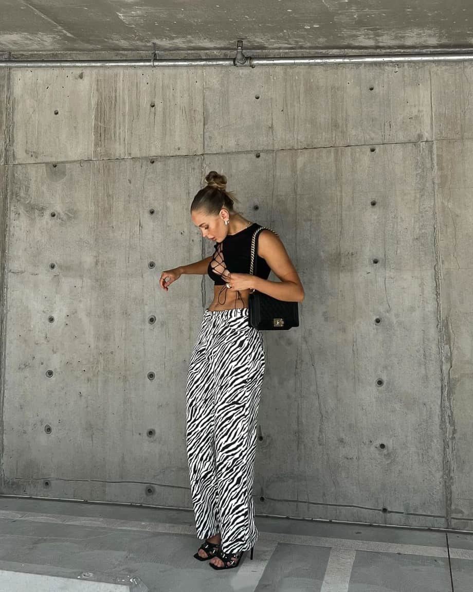 A woman wearing zebra pants with a black cut-out crop top, black heels, and a black purse