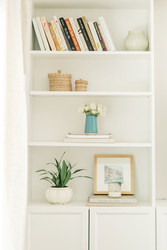 a white shelf with books and a vase of flowers