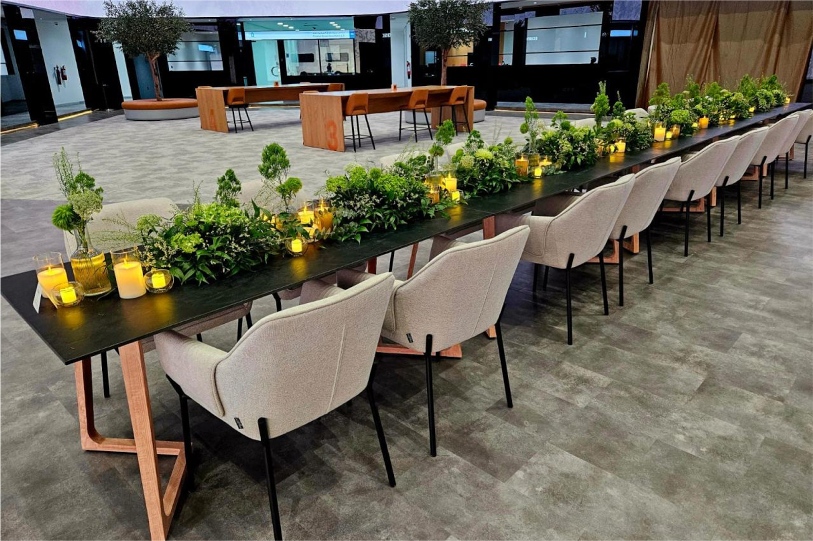 Indoor wedding venue with modern long dining tables, greenery centrepieces, and soft candle lighting.