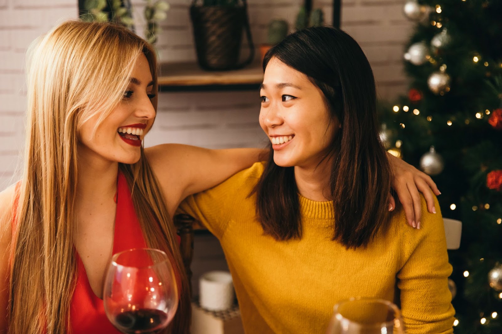 Um casal se abraça sorrindo em um ambiente natalino enquanto tomam vinho.