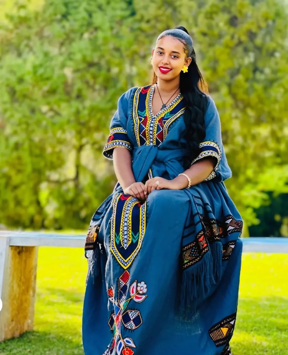 Woman wearing blue Habesha dress with vibrant embroidered patterns and netela