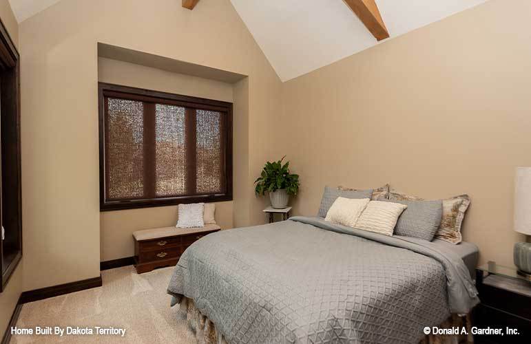 Bedroom with a vaulted ceiling, a skirted bed, and a trio of windows fitted against the inset wall.
