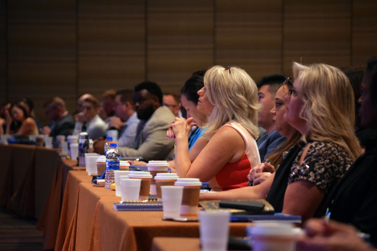 People seated at a long table, attentively participating in a training session, with notebooks in front of them.