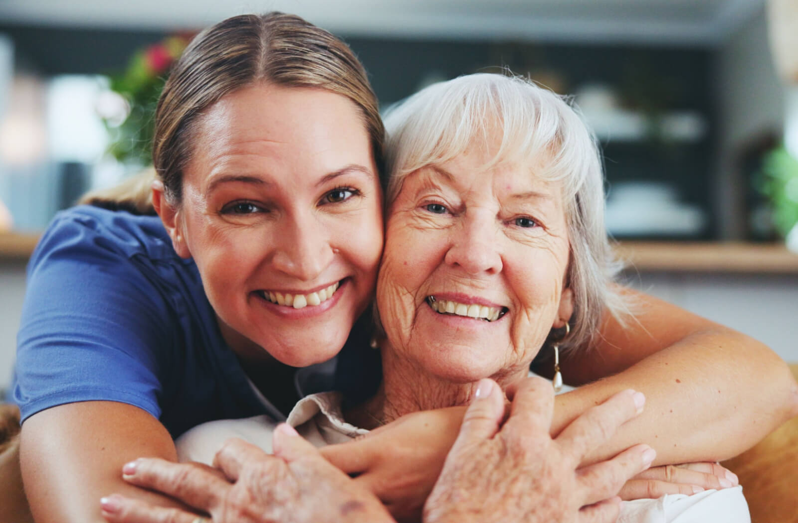 A caregiver in memory care hugging an older resident from behind while both smile.