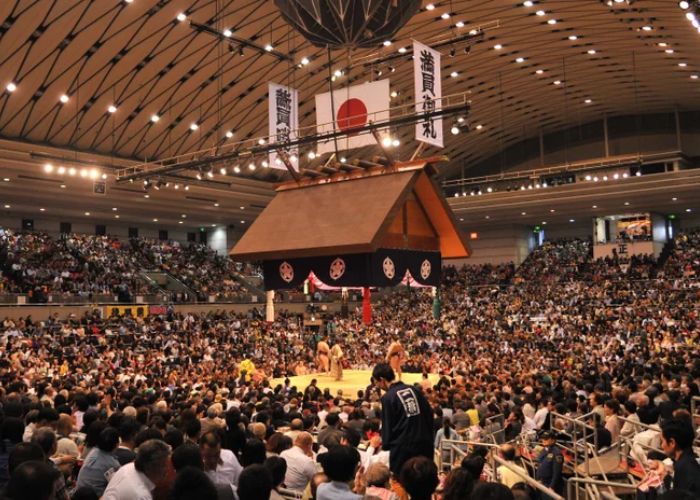 A packed stadium where people are watching the Osaka Grand Sumo Tournament