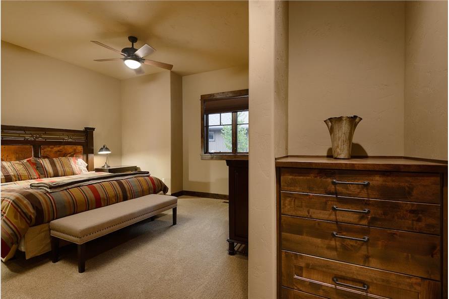 Bedroom with beige walls, wooden dressers, and a cozy bed paired with a long bench.