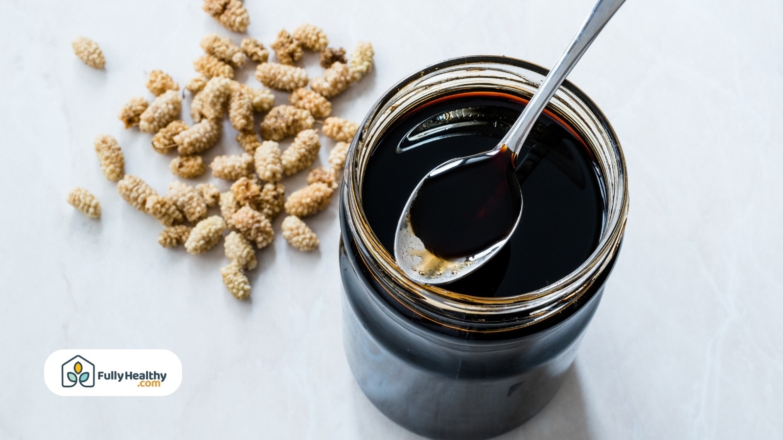 Dark molasses in jar with spoon beside dried white mulberries.