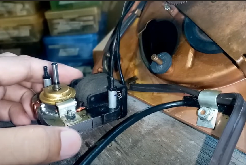 A hand holding a small motor component from a turntable during a repair.