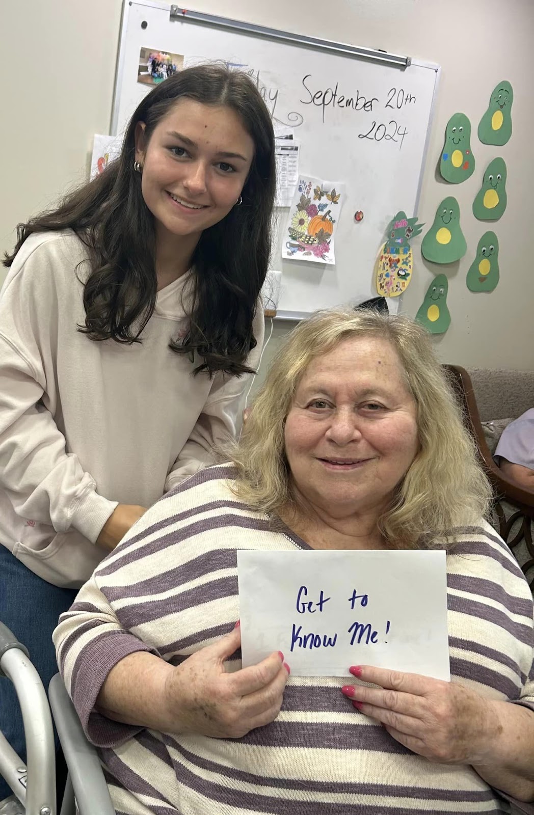 A woman in a wheelchair smiling with a sign while a school-aged student stands behind her