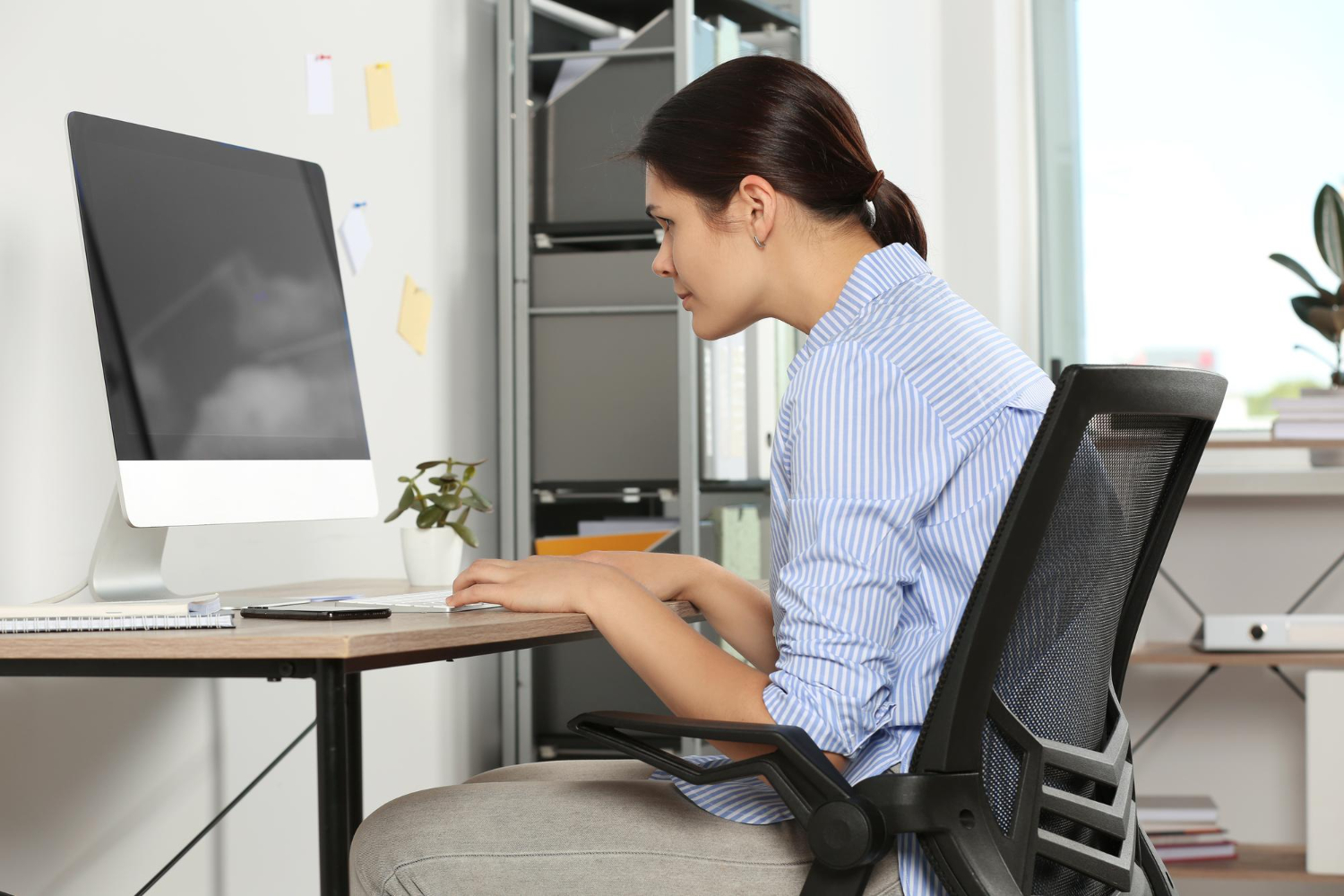 A woman hunches over her computer with poor posture, an example of an ergonomic hazard that office risk assessment consulting can fix.