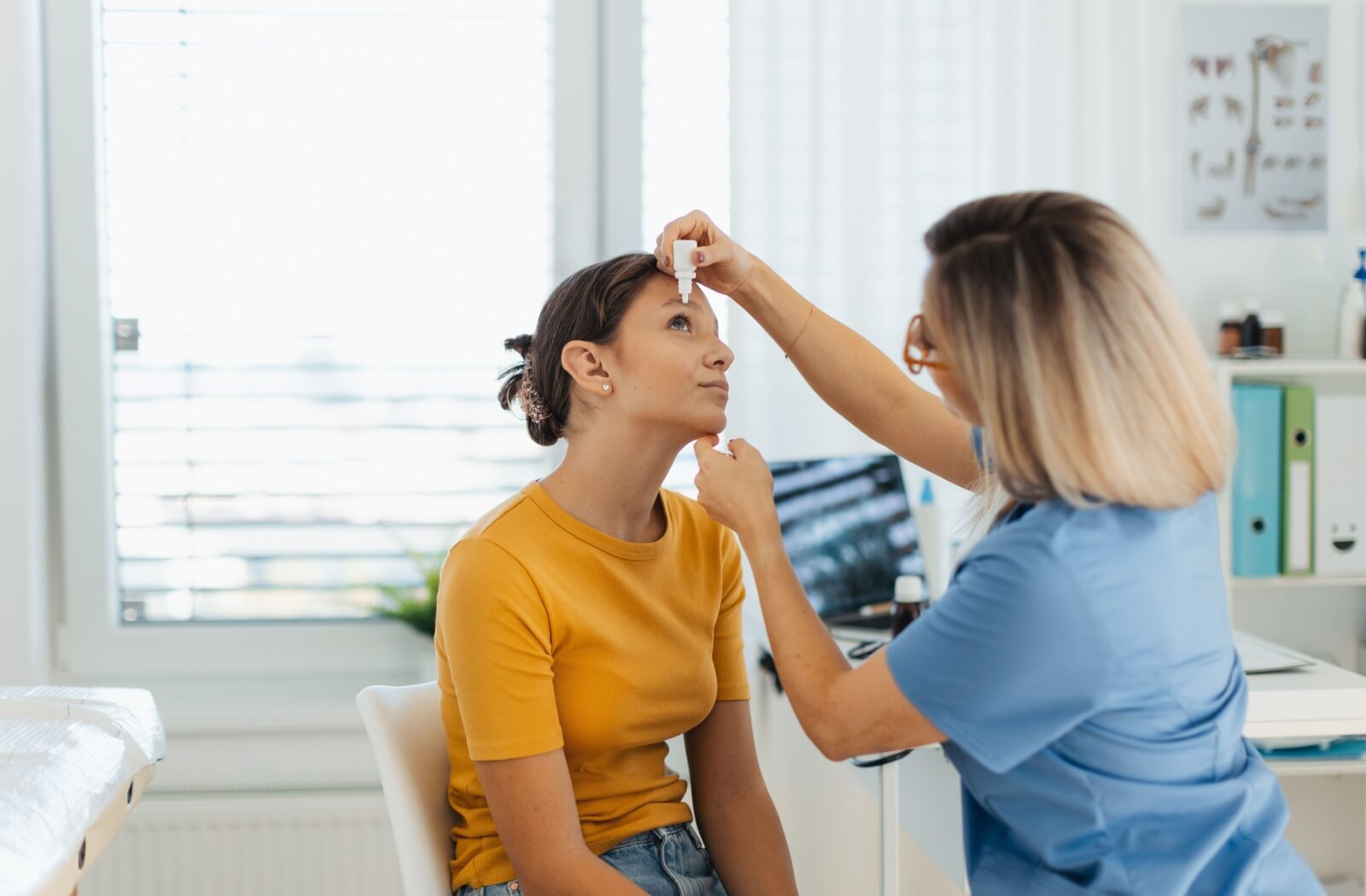 A doctor applies eye drops to a young woman's dry eyes.