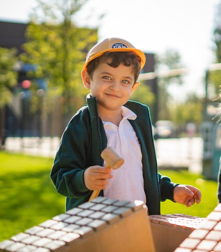 A child holding a mallet and brick wall

Description automatically generated