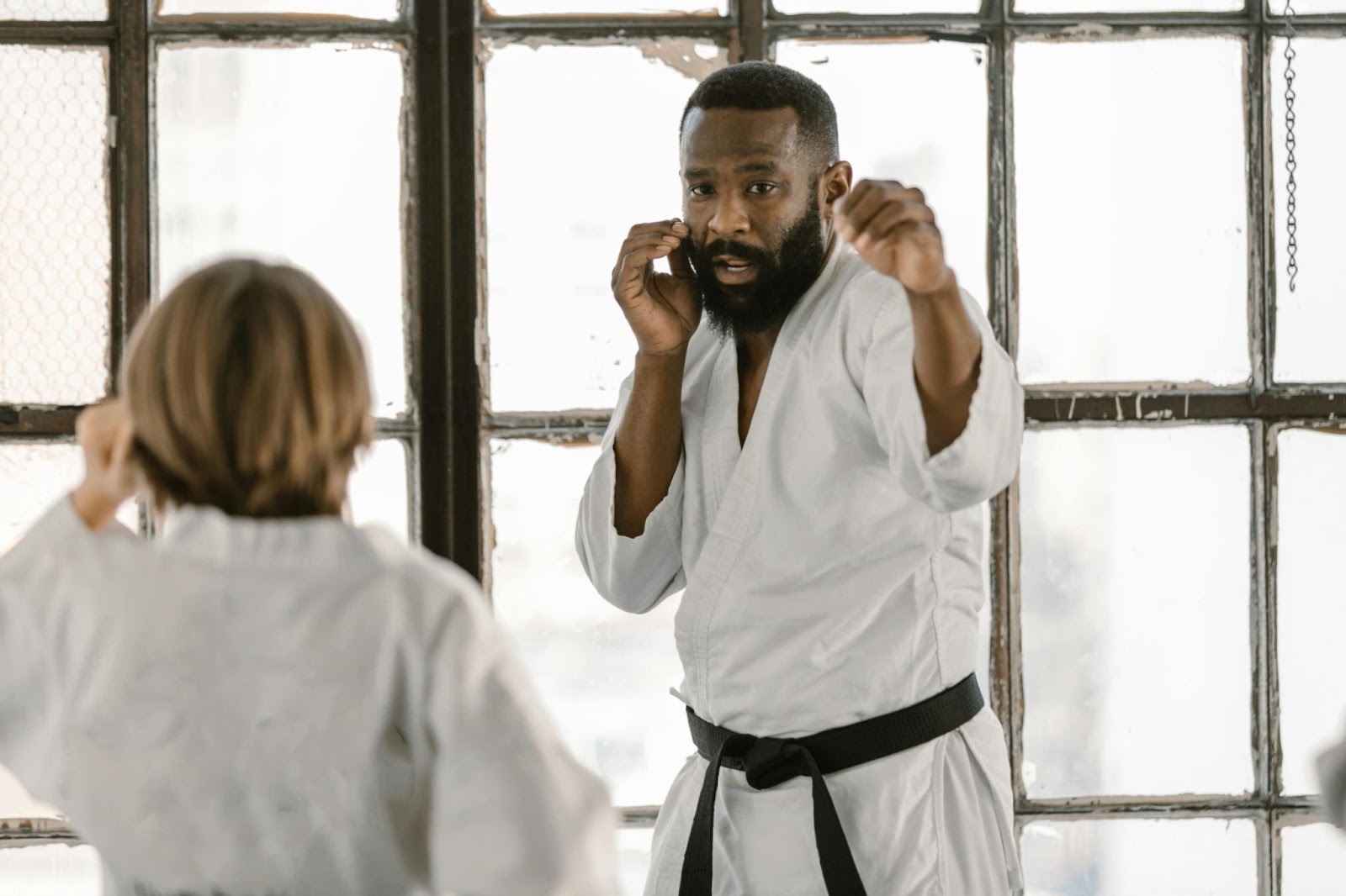 A martial arts instructor demonstrating a defensive move to a young student, with one hand positioned to block.