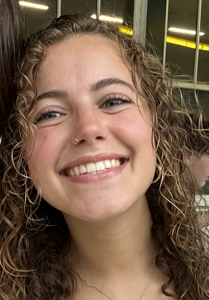A head portrait of a smiling young woman with curly, long, light brown hair.