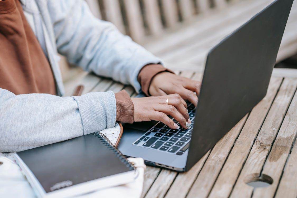 Free Crop female entrepreneur typing on portable laptop while working in park Stock Photo