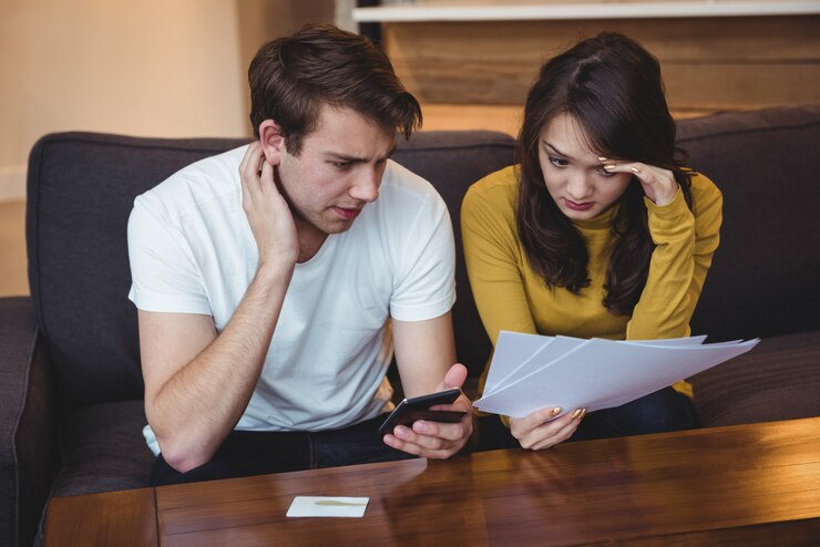 [A couple sitting on a couch, reviewing financial documents and looking stressed]