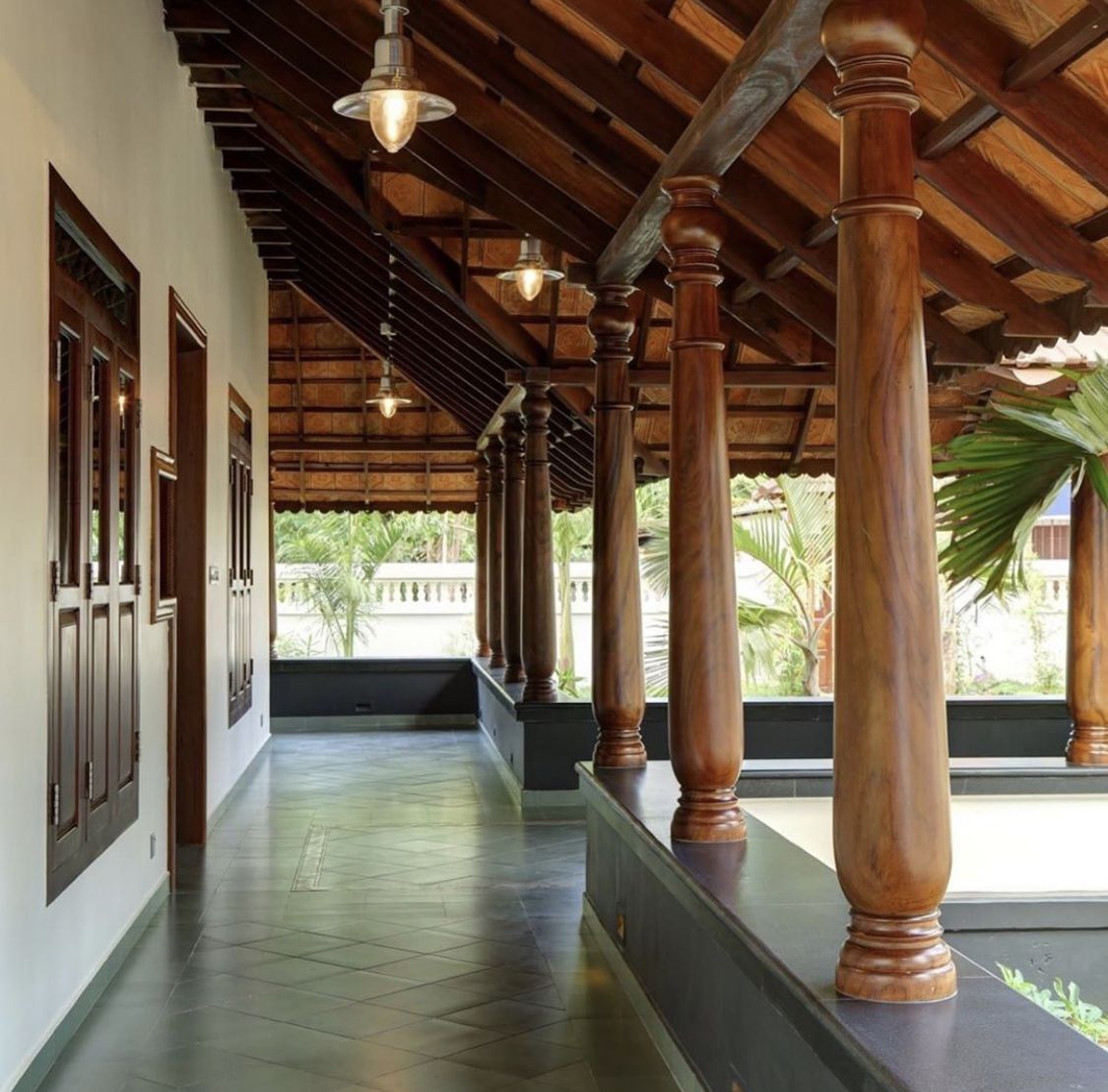 A covered outdoor walkway veranda, with a polished wooden ceiling and large wooden columns showcases traditional architecture.