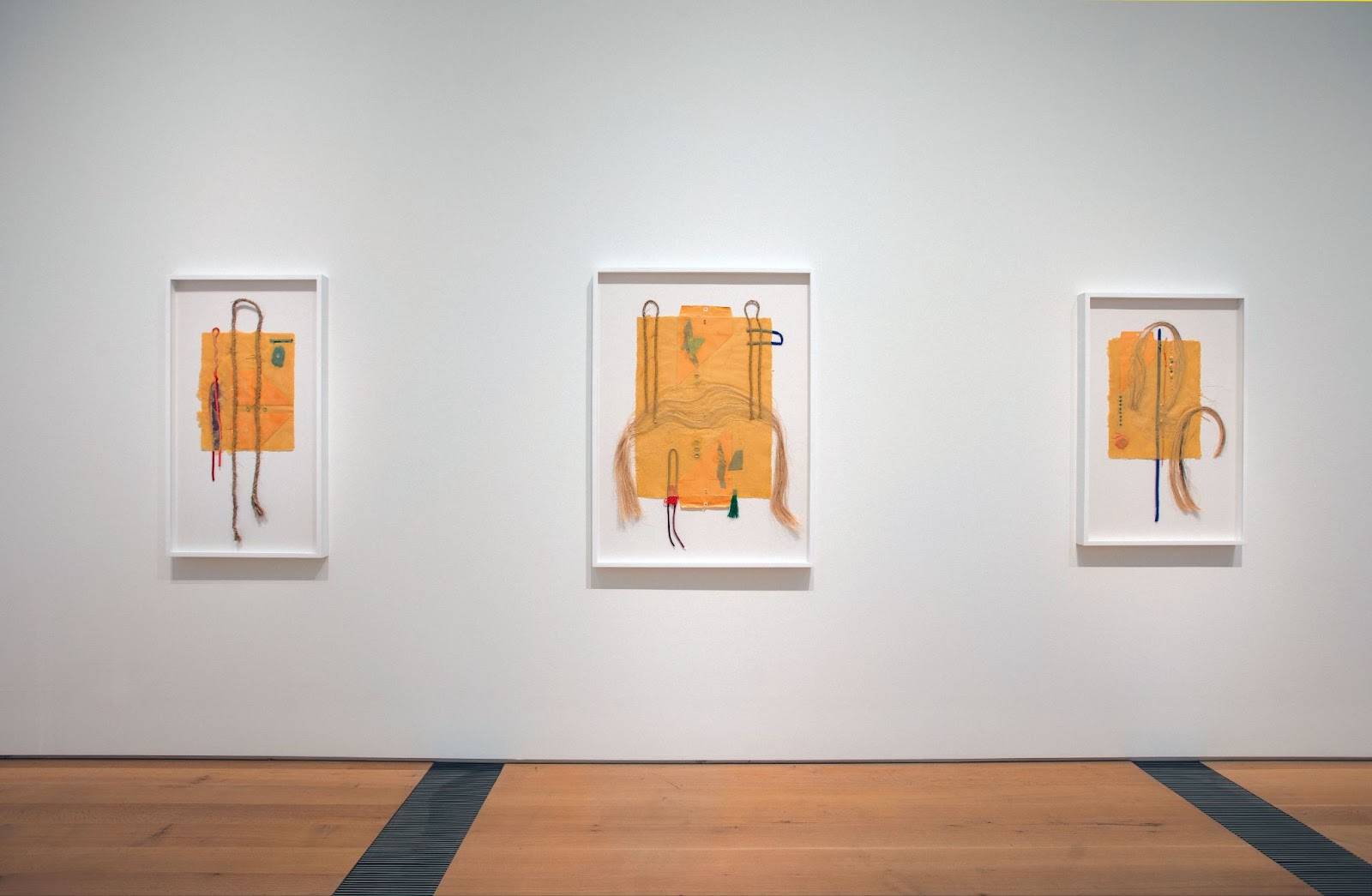 Image: Installation View, "Currents 124: Crystal Z Campbell," Saint Louis Art Museum, 2024. Three abstract works on a white wall hung in a gallery of hair and other materials with yellow envelopes. Courtesy of the artist.
