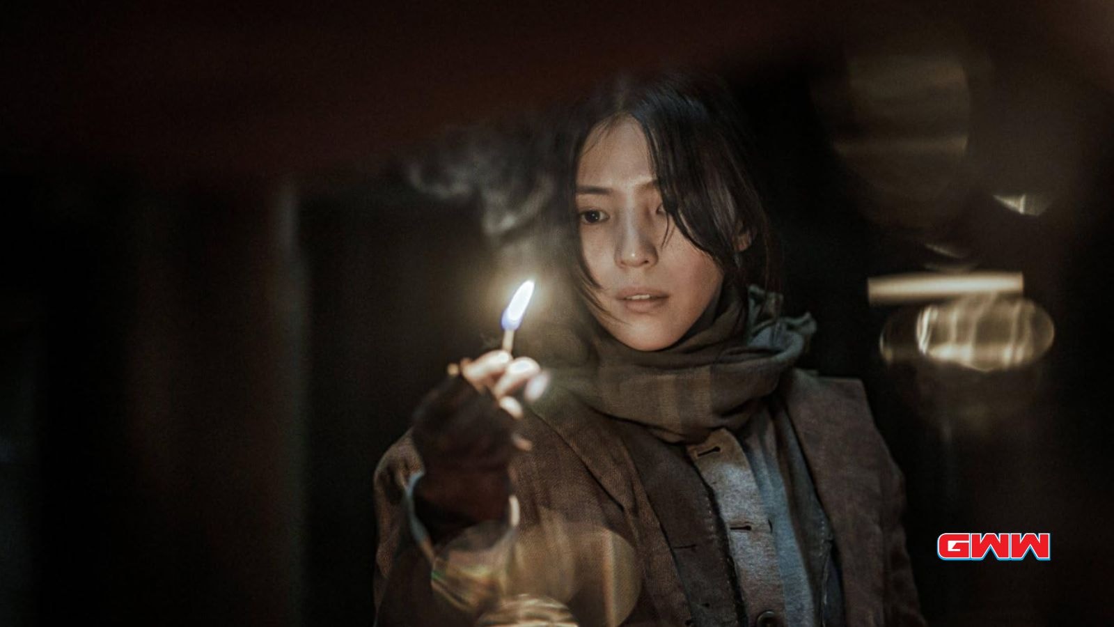 Yoon Chae-ok holding a lit match while exploring a dark, mysterious room.