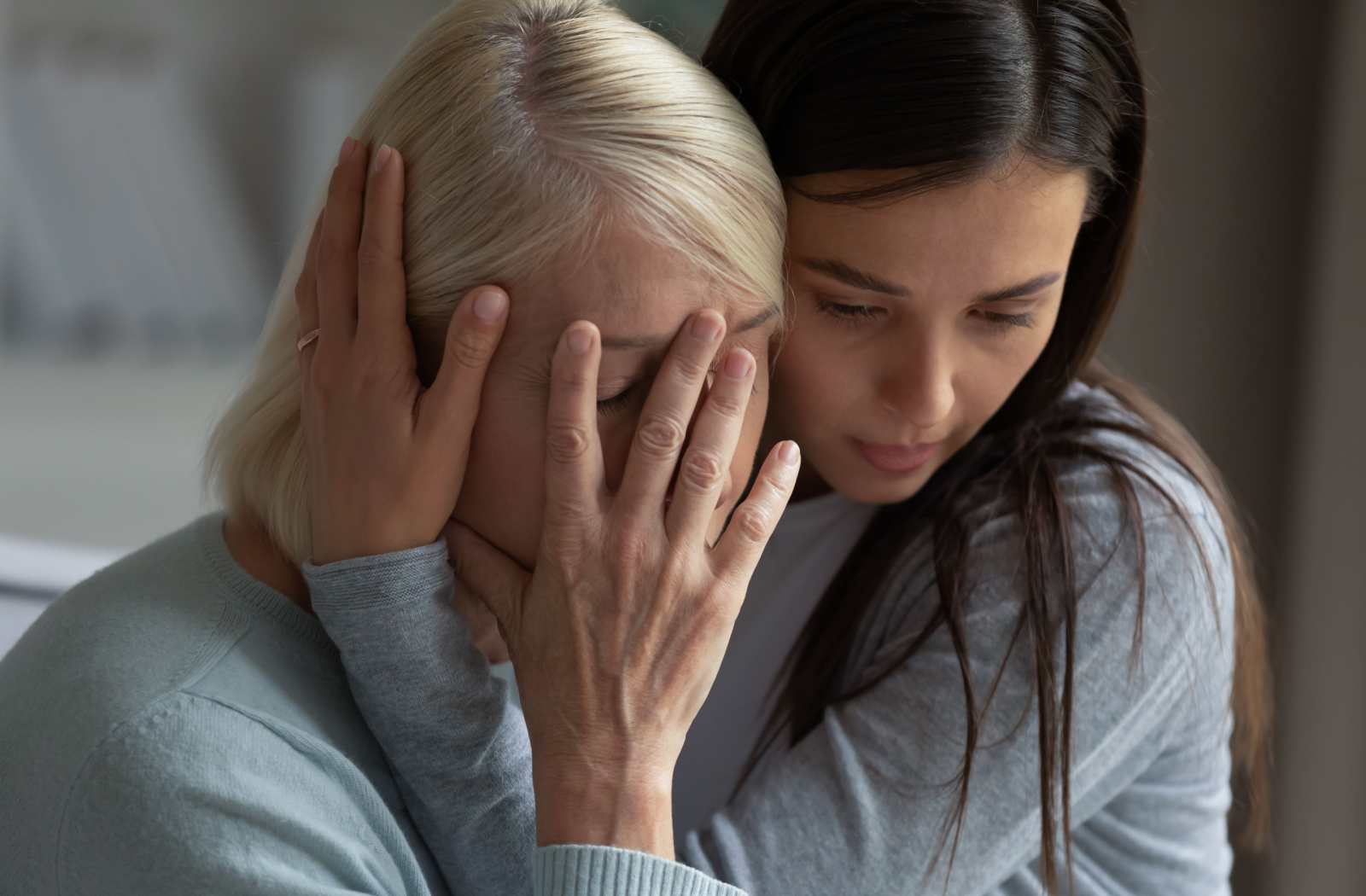 An adult child comforts their senior parent with memory loss in a close embrace.