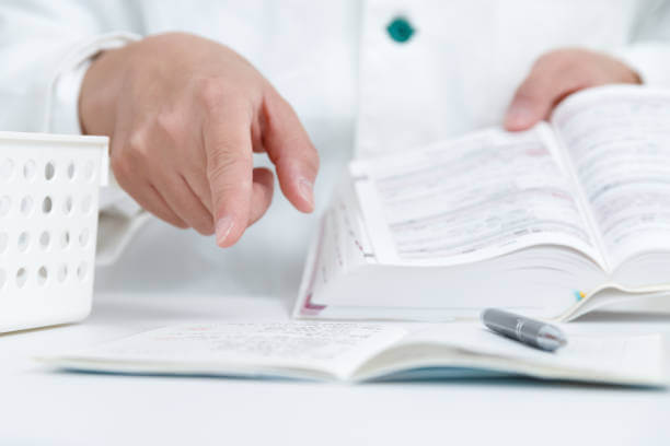 A focused pharmacist reading a medical reference book to ensure compliance with safety standards in the preparation of compounded medicine.