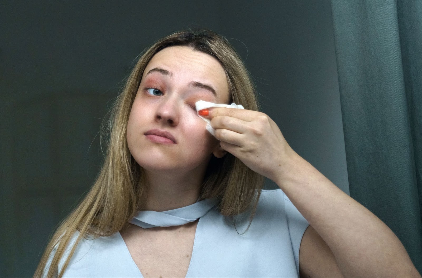 A person wipes the upper eyelid of one of their left eye with a cotton cloth to remove any built-up dirt or makeup.