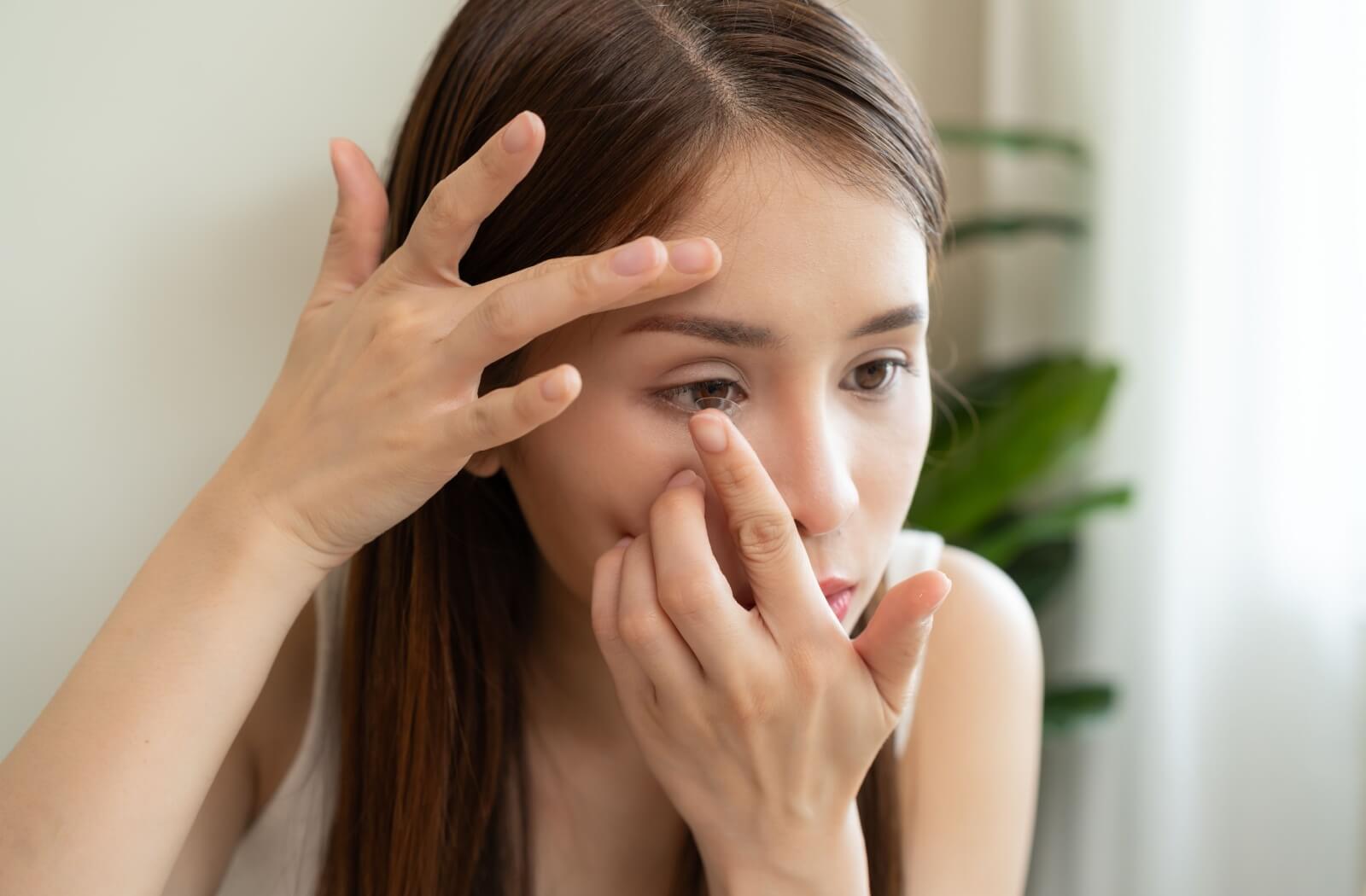 Woman inserting a contact lens into her eye in front of a mirror.