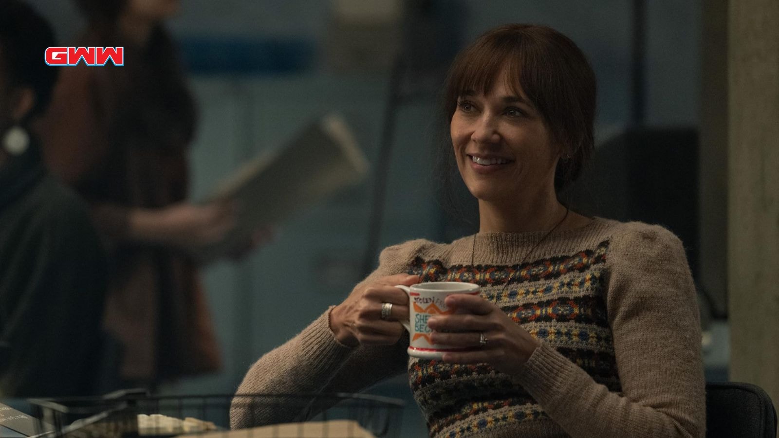 Martha smiling while holding a mug, sitting in a dimly lit room.