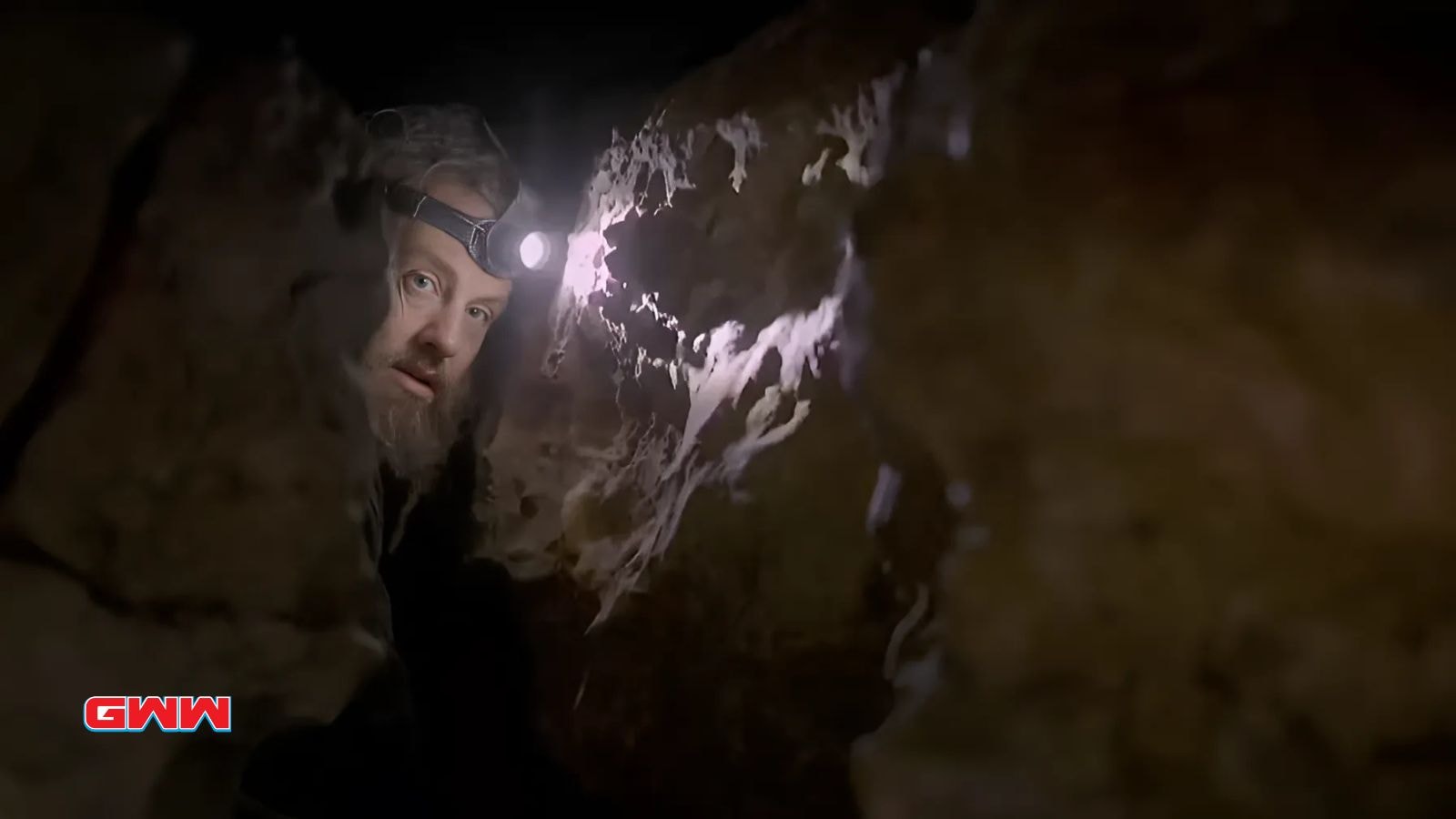 Charlie Snider examining mysterious rock formation within a dark cave