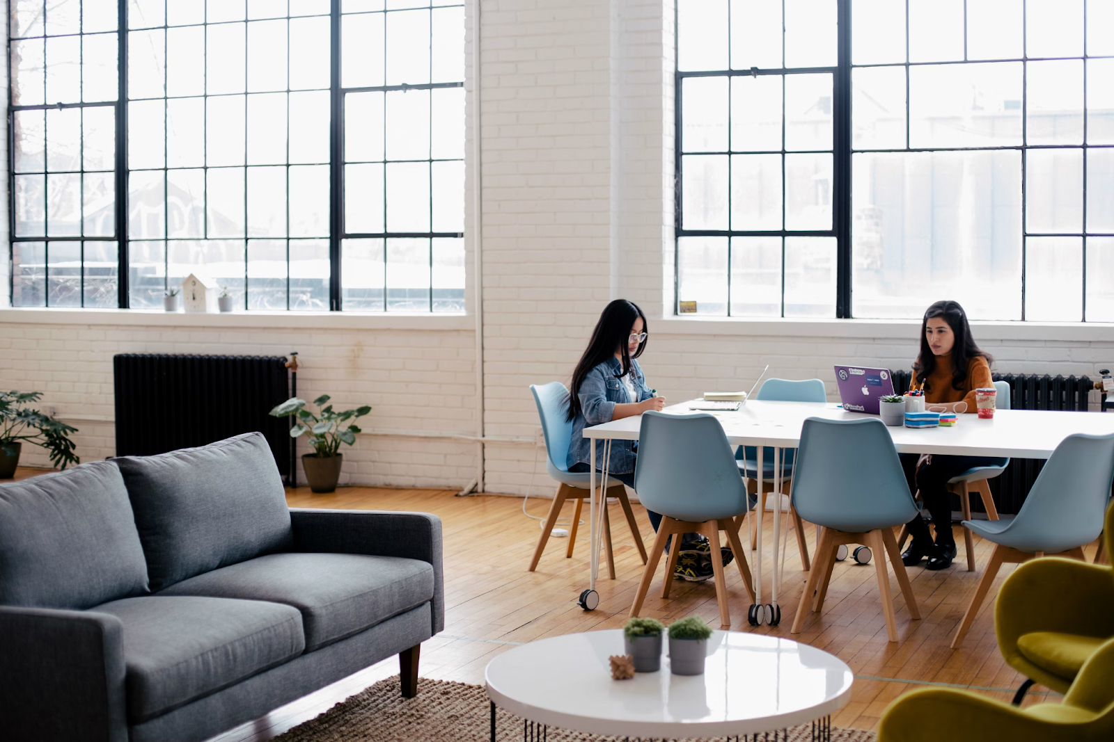 Two women in an office with tables, chairs, and plants 