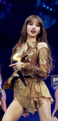 This  contain an image of Lisa the singer is dressed in gold and holding a microphone