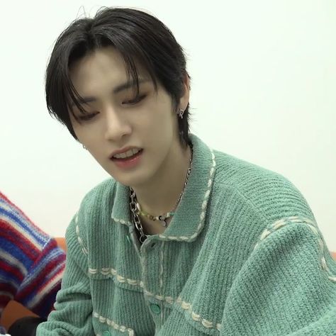 This  contain an image of TRCNG's Taeson in a green sweater looking at his cell phone while sitting next to another person