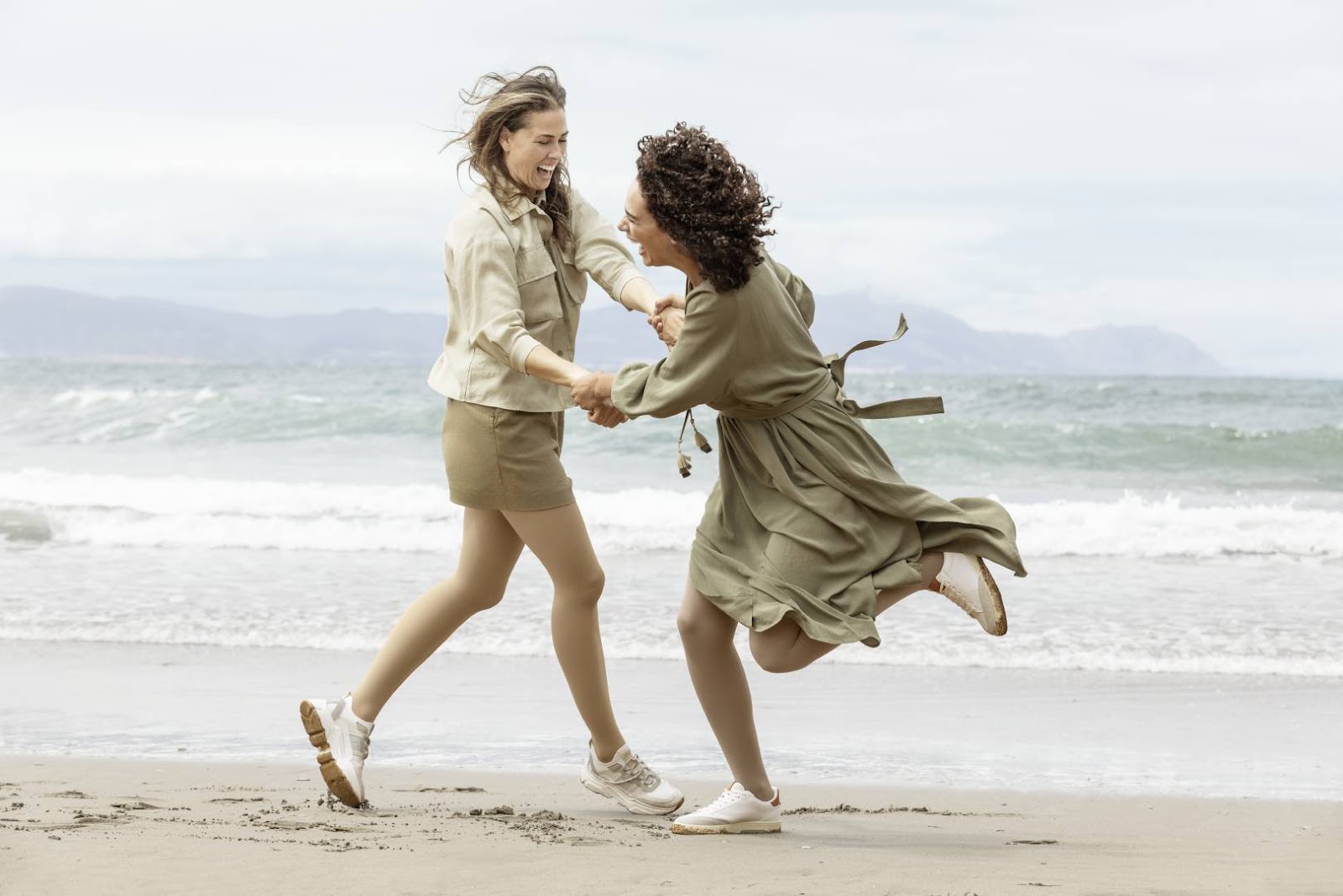 Two women dancing together on the beach. They are both wearing Bauerfeind compression stockings