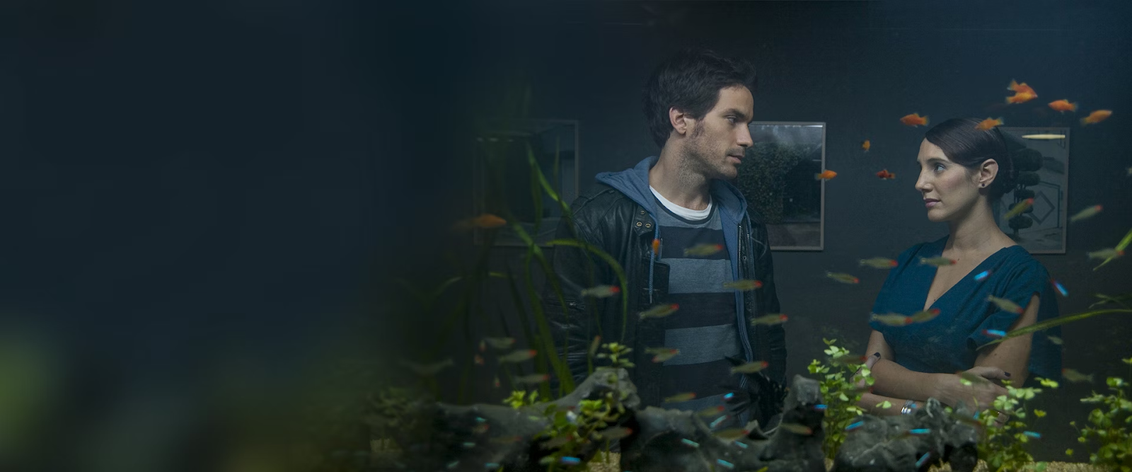 Santiago Cabrera en La Vida de los Peces, interactuando con Blanca Lewin frente a un acuario iluminado.