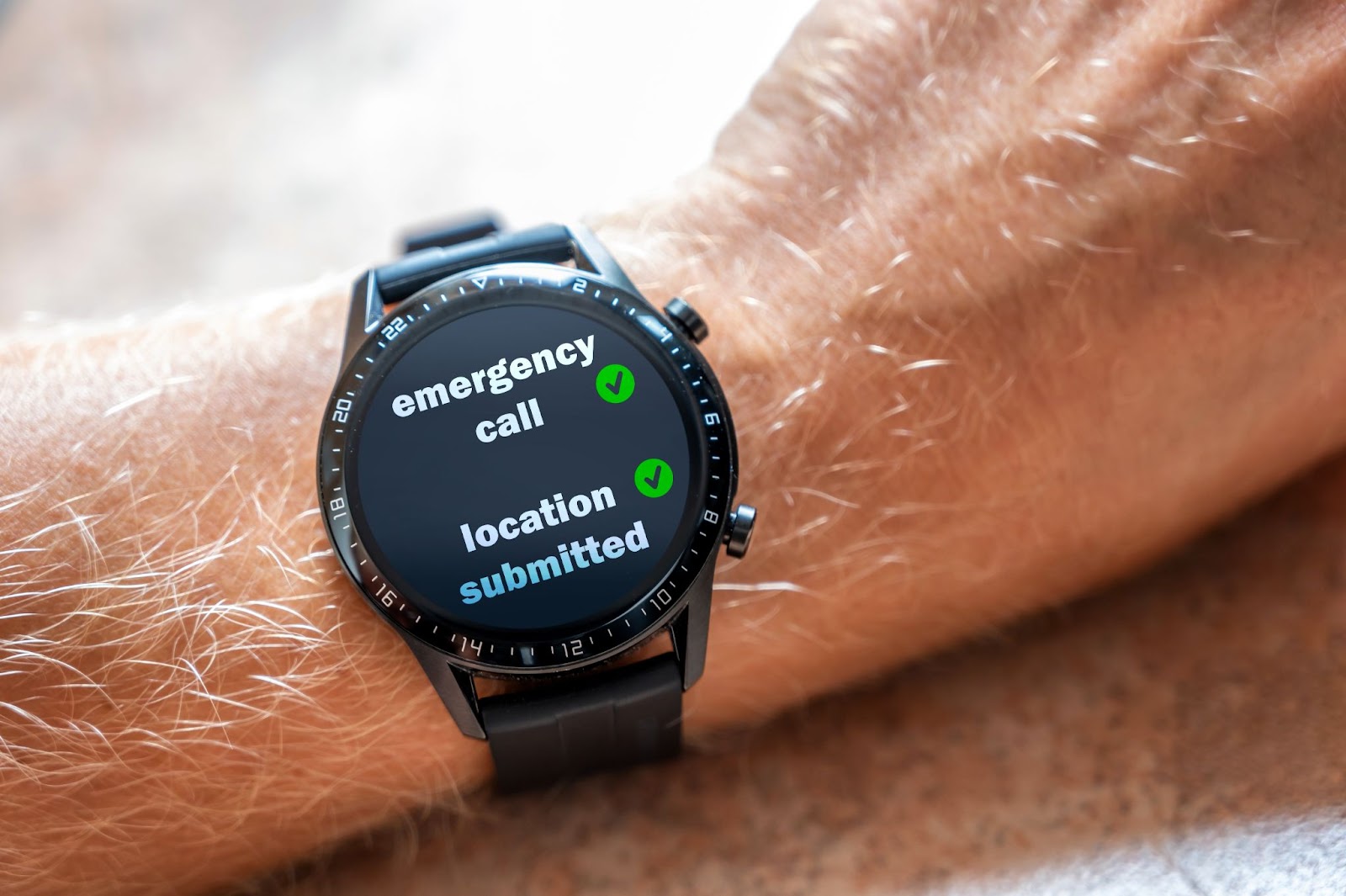 A close-up of an older adults wrist with a fall detection watch displaying emergency call and location submitted text.
