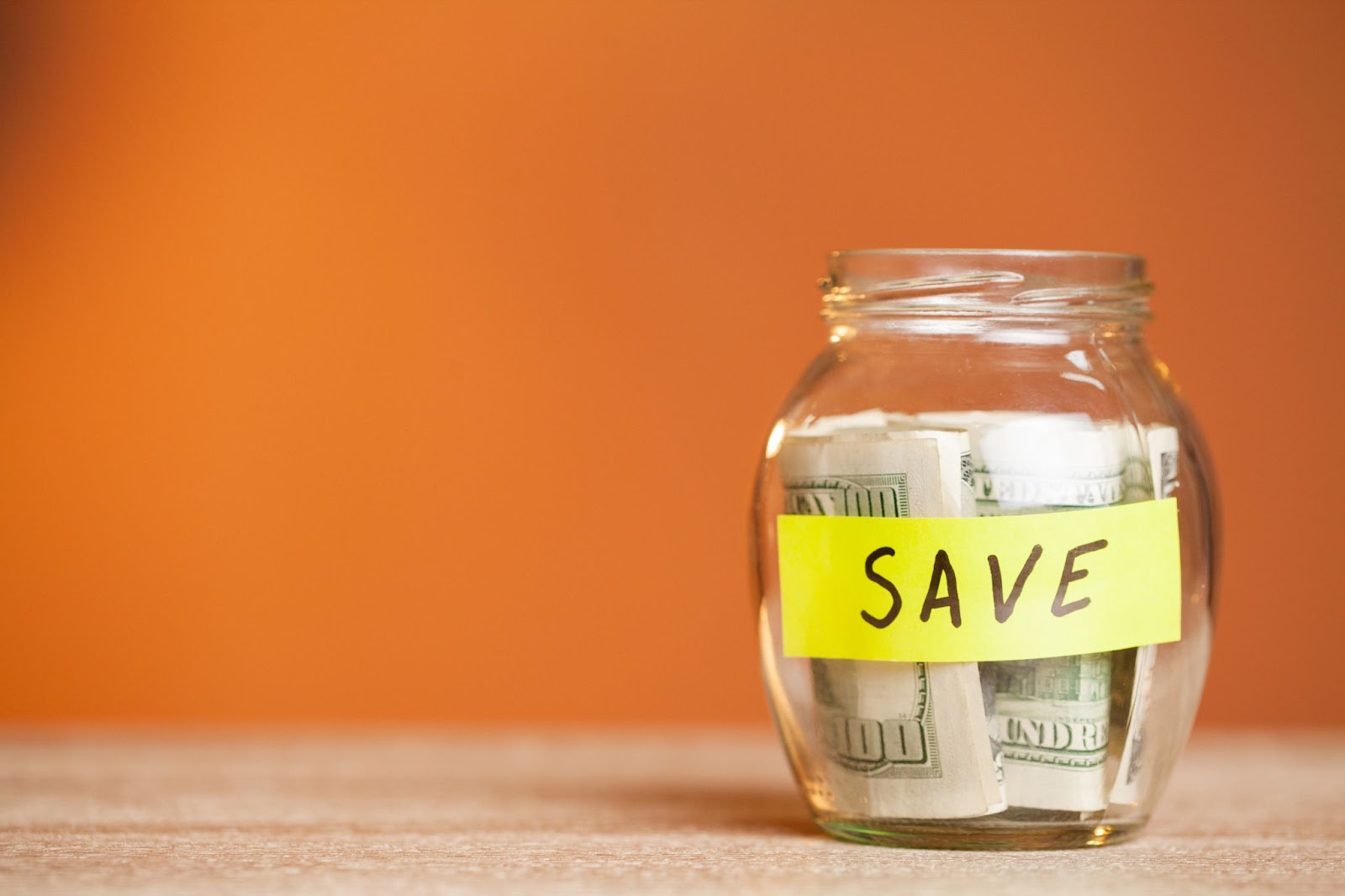 Word “save” on a jar with money in it on a wooden surface. 