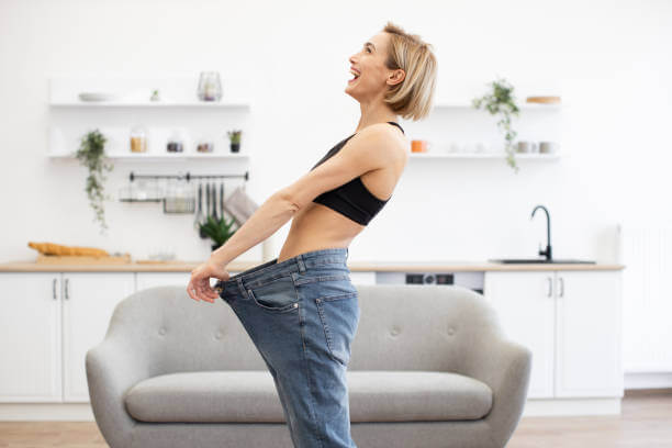 Happy woman celebrating weight loss success, wearing loose-fitting pants after reducing cortisol.