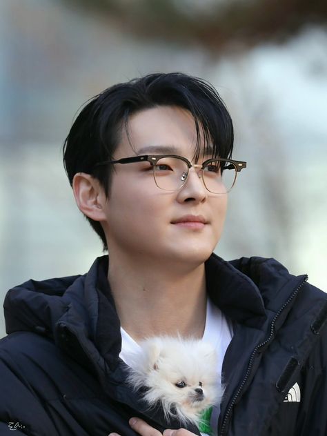 This contain SF9's Zuho with glasses holding a small white dog in his arms and looking off to the side