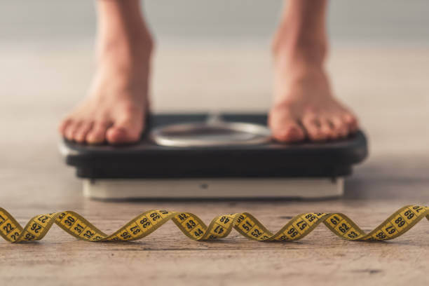 A woman standing on a scale, checking her weight while monitoring her health and wellness.