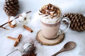 A glass cup of hot chocolate with whipped cream and cinnamon sticks

Description automatically generated