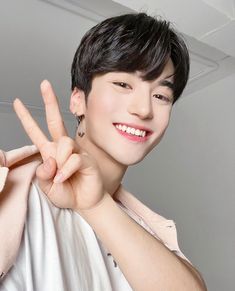 This contain Beomhan making the peace sign with his hand while wearing a white shirt and earrings