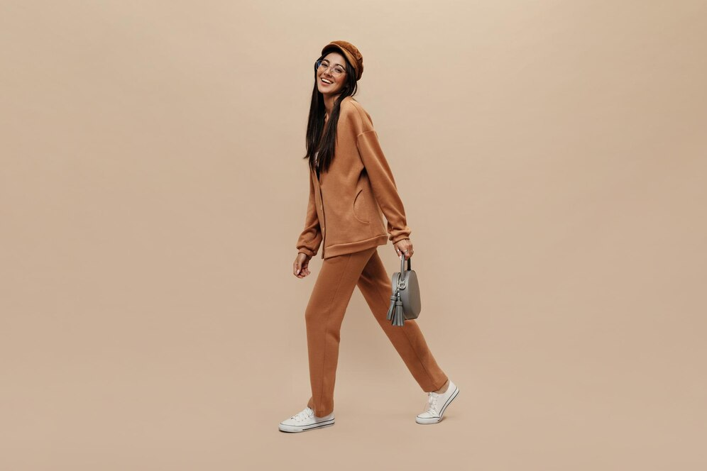 seorang wanita dengan style monokrom warna cokelat tersenyum sambil membawa tas