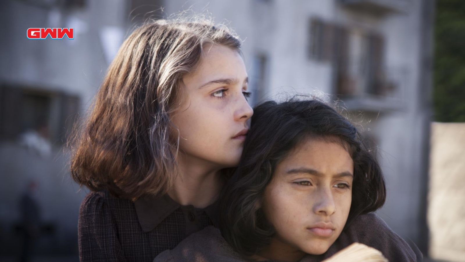 Elena and Lila embrace, looking distant and contemplative, in a somber setting.