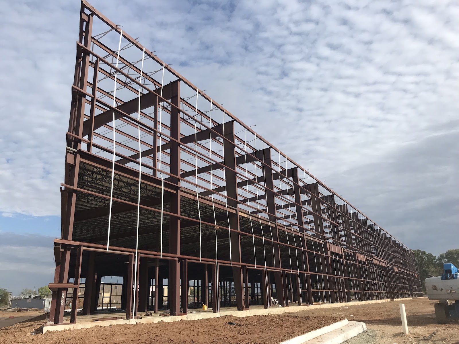 Steel framework of an industrial building under construction against a partly cloudy sky.