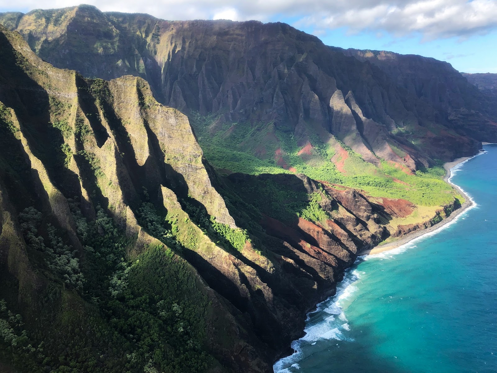 A breathtaking aerial view of Kaua‘i’s Nāpali Coast, featuring lush green cliffs and crystal-clear ocean waves.