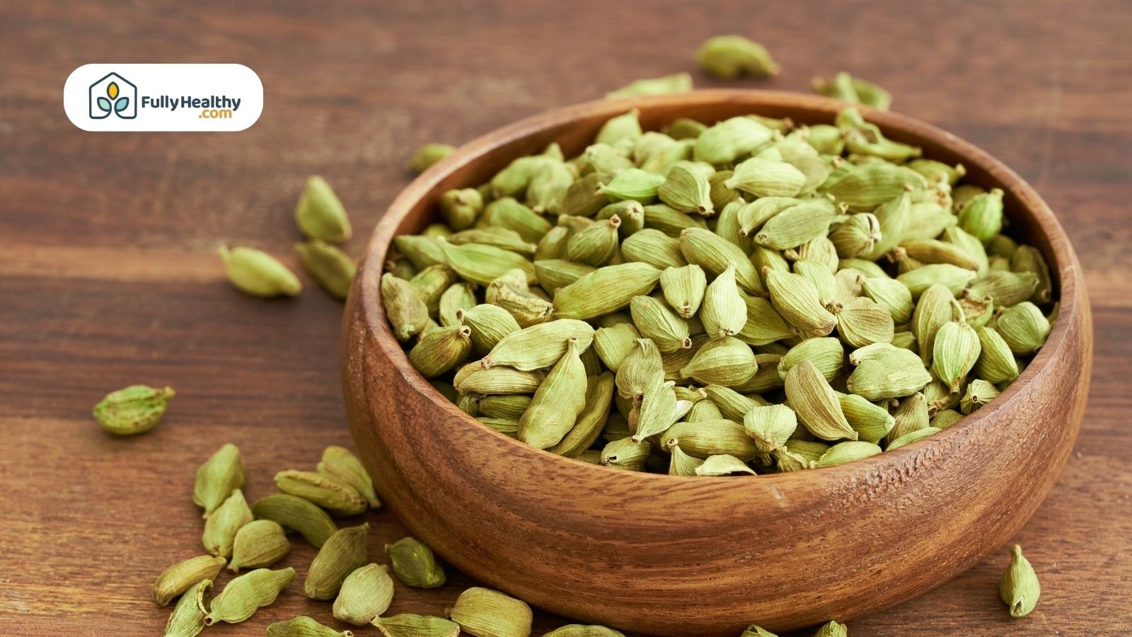 Wooden bowl filled with green cardamom pods on wooden table