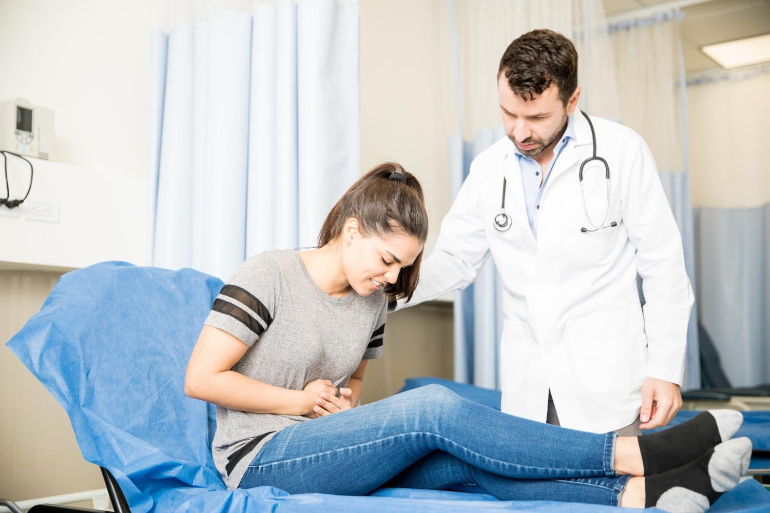 pasien wanita mengeluh nyeri perut saat berkonsultasi dengan dokter urologi di ruang pemeriksaan rumah sakit.